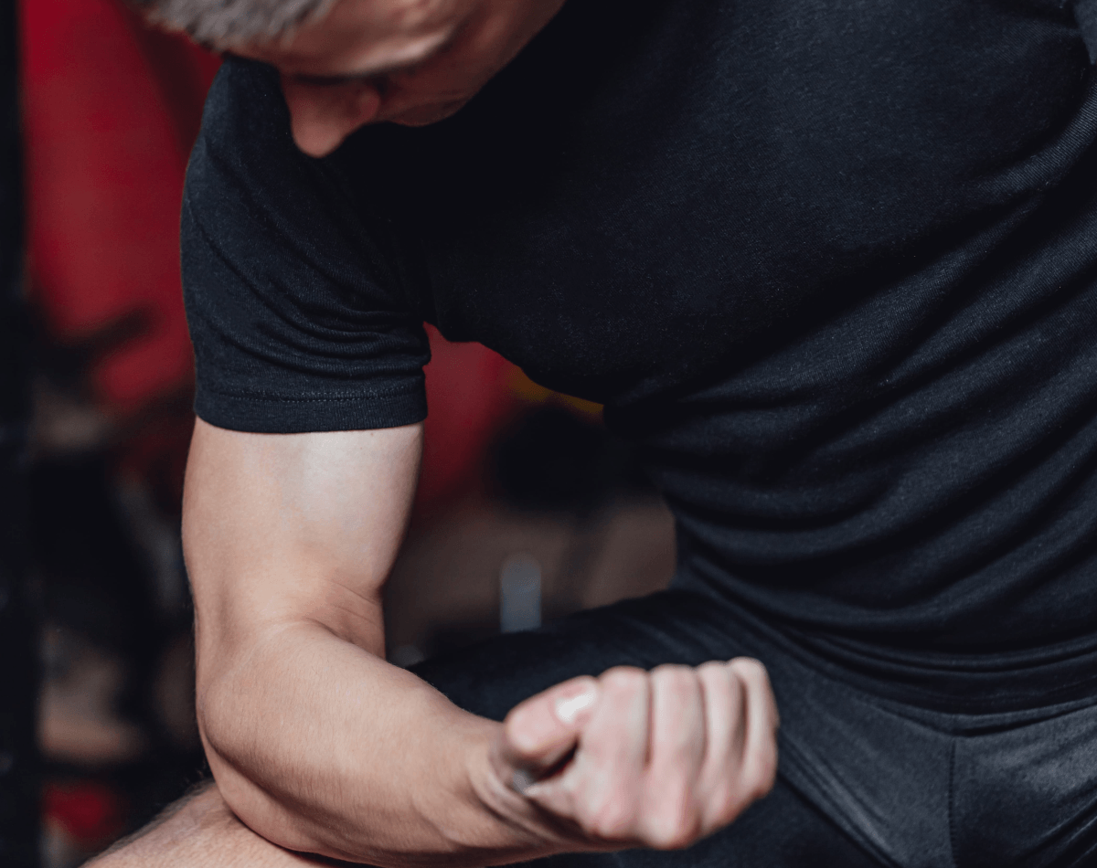 Male athlete assessing elbow pain while resting elbow on knee and flexing extending elbow