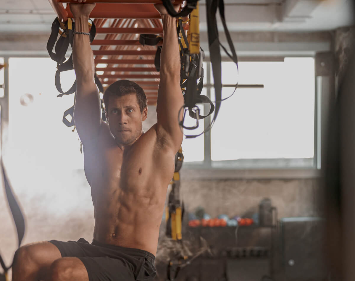Shirtless muscular man doing dead hangs at the gym to fix tennis elbow issues
