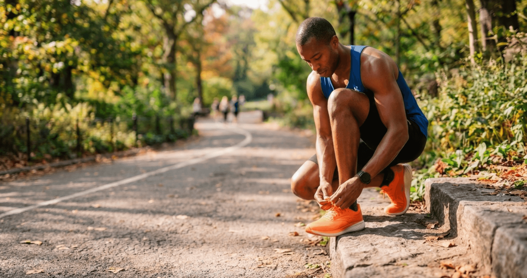 An athlete in a blue tank top and black shorts, after applying Battle Balm all natural & organic topical pain cream, crouches on stone steps beside a park path, tying his shoelaces and preparing for a run.